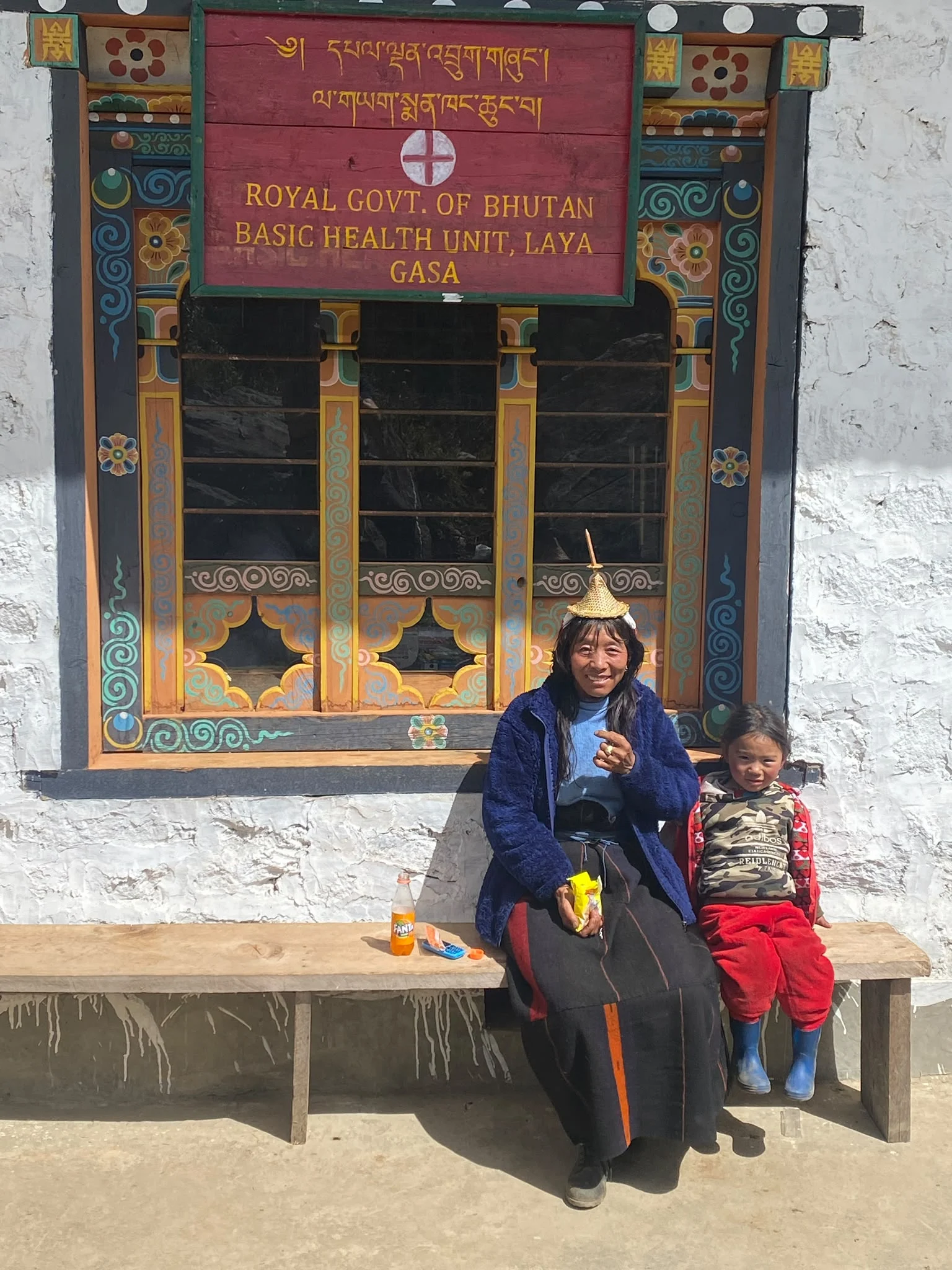 A woman and child seated outside the Basic Health Unit in Laya, Bhutan
