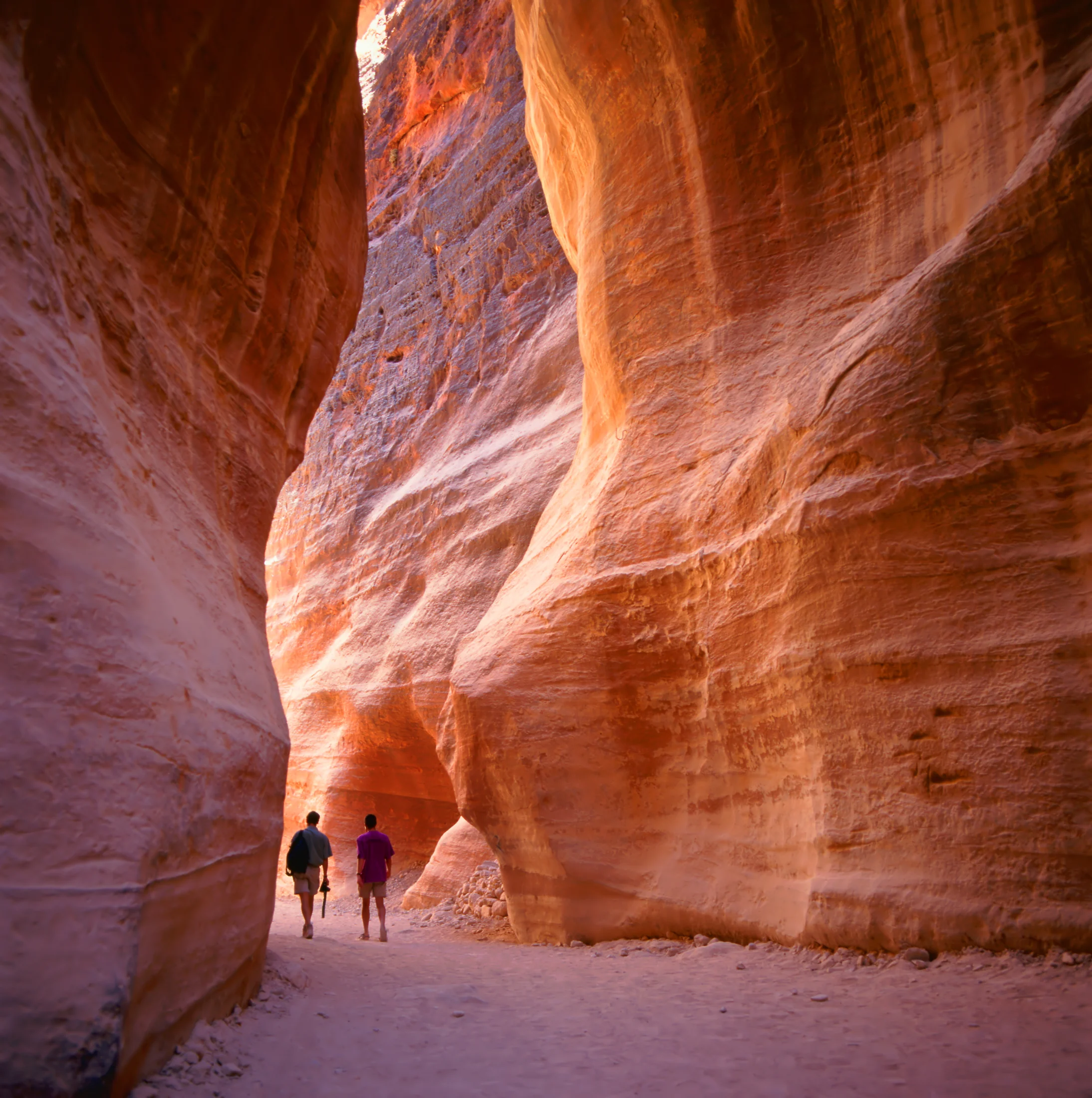 Two people walking through a monumental sandstone passage at Petra